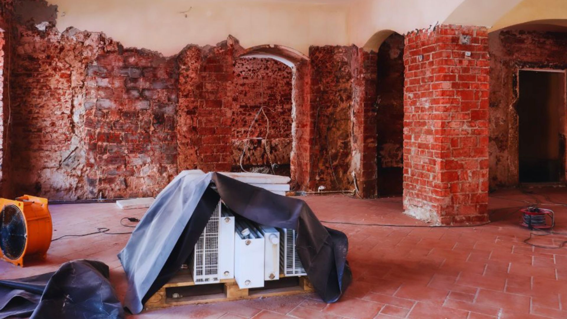 Industrial fans and restoration equipment are set up inside a room with exposed brick walls and damaged surfaces, showing the process of fire damage restoration and cleanup.
